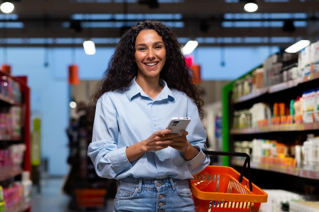 Photo shopping in a supermarket a young latin american woman stands between rows of shelves with a cart he