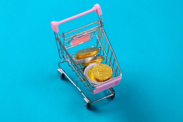 Shopping theme. Mini Supermarket trolley with coins on blue