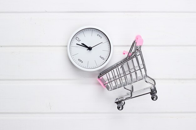 Shopping time. Supermarket trolleys with clock on white wooden surface. Minimalism. Top view