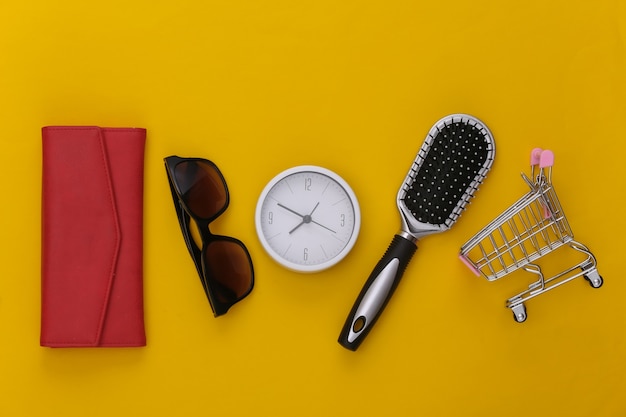 Фото Время для покупок. женские аксессуары. бумажник, расческа, солнцезащитные очки и часы, тележка супермаркета на желтом.