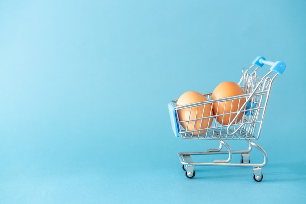 Shopping toy trolley with eggs on blue background concept