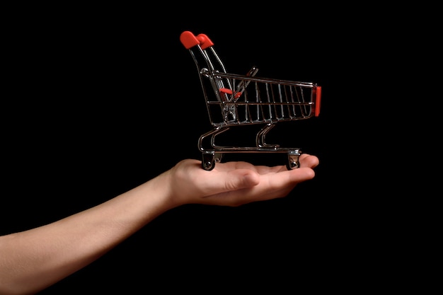 Shopping trolley on a child's palm on a dark background. Shopping concept