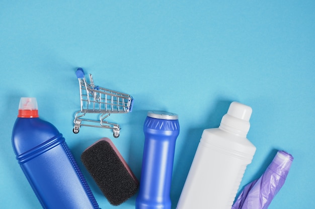 Shopping trolley and detergent bottle without labels on blue background cleaning set. top view. cleaning service concept