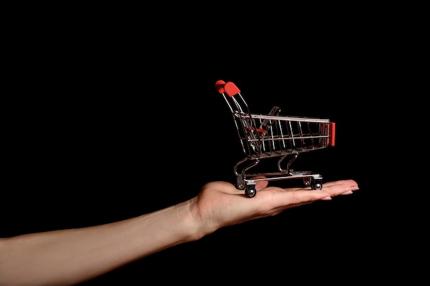 Shopping trolley on female palm on dark 