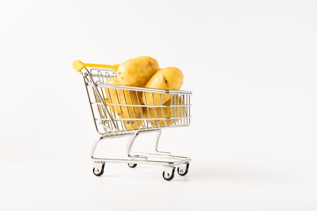 Shopping trolley filled with potatoes on white background