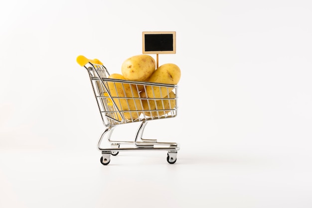 Shopping trolley filled with potatoes on white background