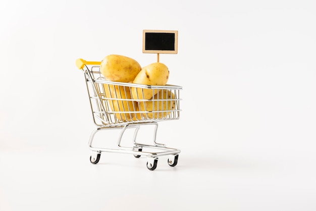 Shopping trolley filled with potatoes on white background