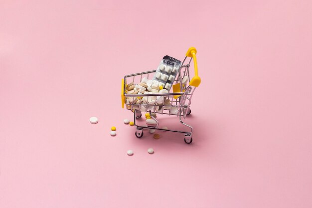 Shopping trolley from the supermarket full of pills and drugs on a pink background. Purchases of medical preparations, purchase on the Internet.