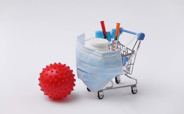 Shopping trolley in medical mask with test tubes, syringes, pills bottle and virus strain model on white background. Healthcare