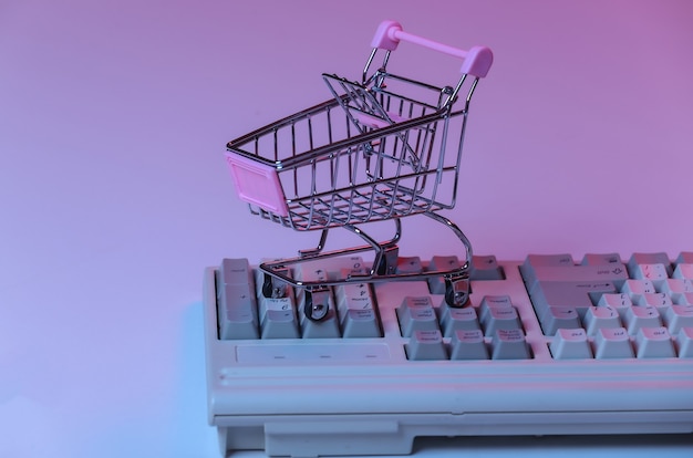 Shopping trolley on old pc keyboard. pink blue gradient neon, holographic light. retro online shopping