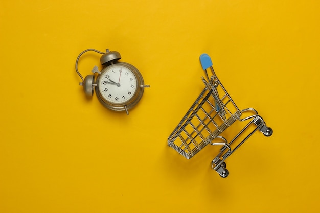 Photo shopping trolley and retro alarm on yellow background. 11:55 am. new year.