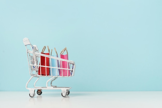 Photo shopping in trolley with colorful bags on blue background small white cart  copy space