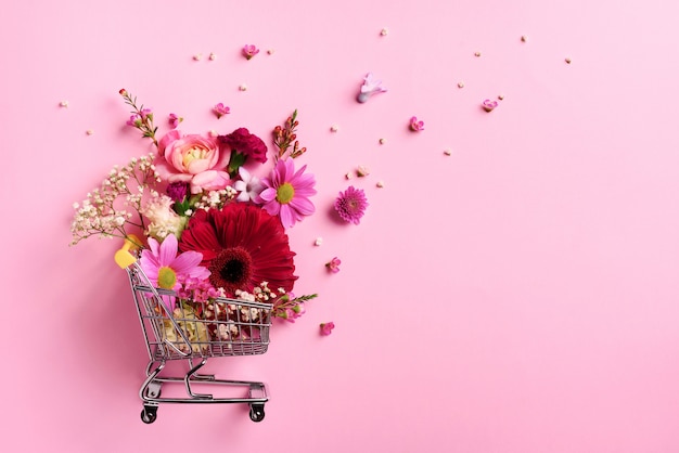 Shopping trolley with flowers on pink punchy pastel background. 