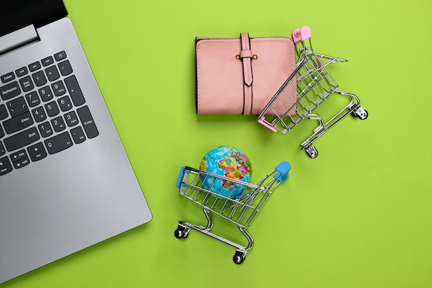 Shopping trolley with globe, wallet, laptop on green