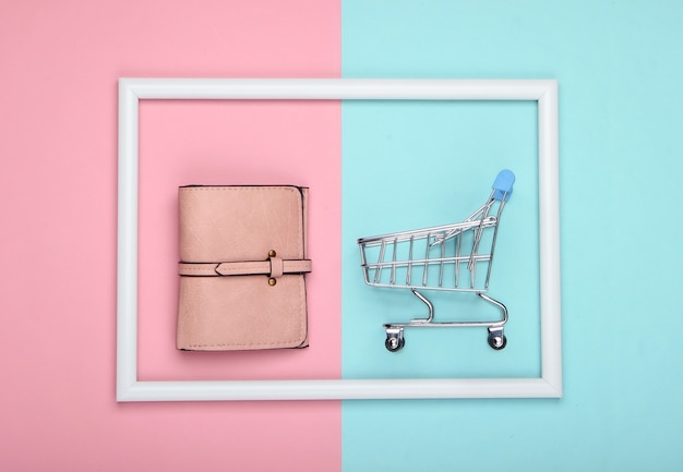 Shopping trolley with leather wallet in a white frame on pink blue pastel surface