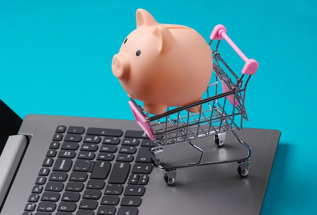 Shopping trolley with Piggy bank on laptop keyboard closeup