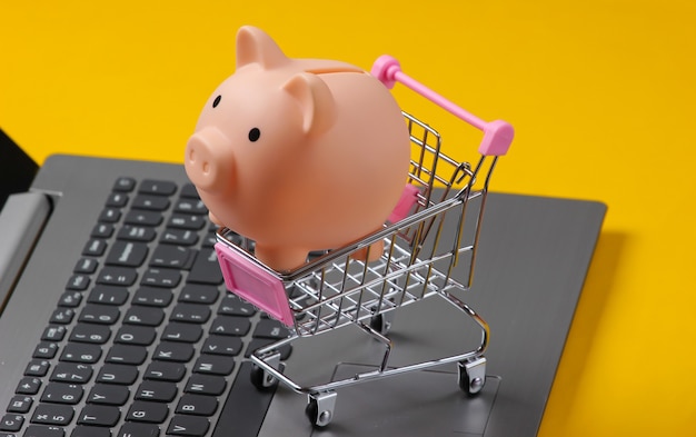 Shopping trolley with Piggy bank on laptop keyboard closeup