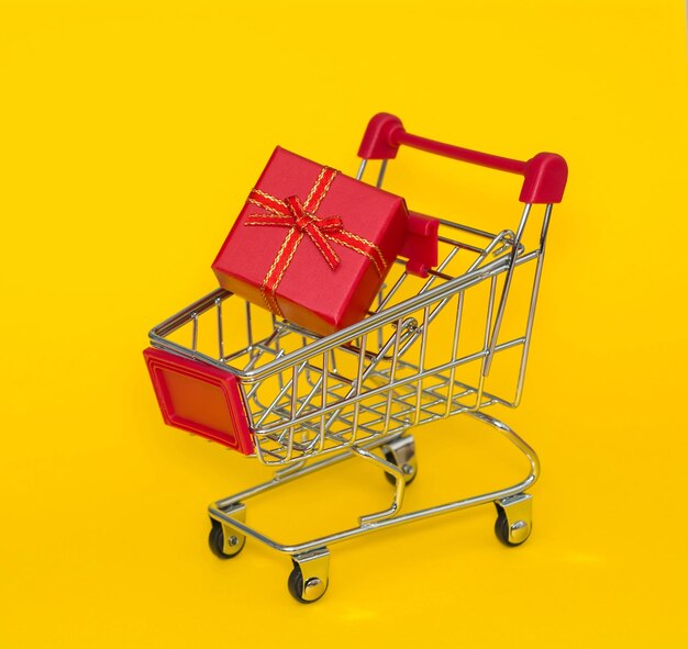 Shopping trolley with red gift on a yellow background