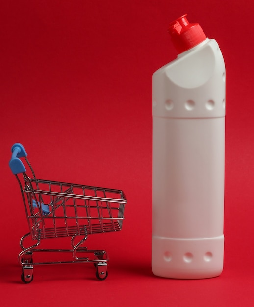Тележка для покупок с белой пластиковой бутылкой моющего средства для ванной и туалета на красном фоне.