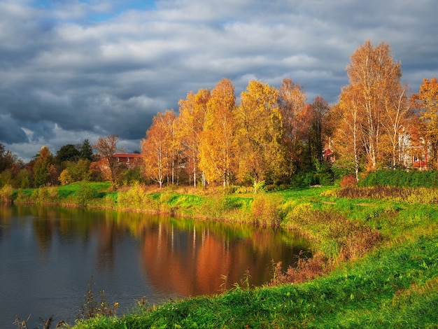 The shore of an autumn lake with the reflection of golden trees in the water. A picturesque autumn landscape with a pond.