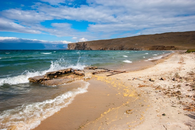 The shore of Lake Baikal with splashes from the waves breaking on stones Sandy shore and rocky cape in the distance