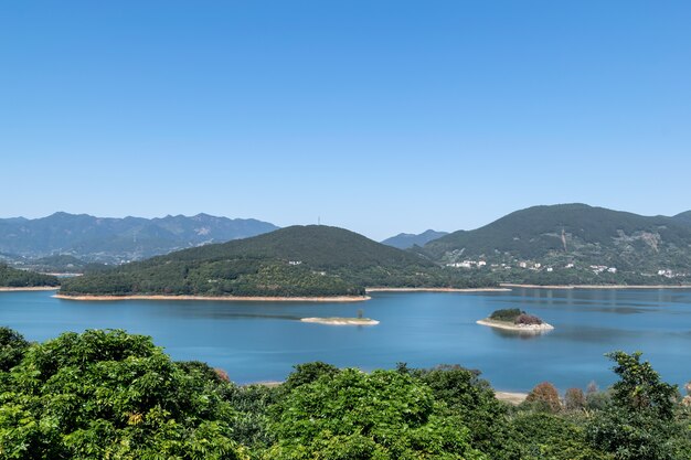 The shore of the lake is green, there are some small islands in the center, and the sky and water are blue