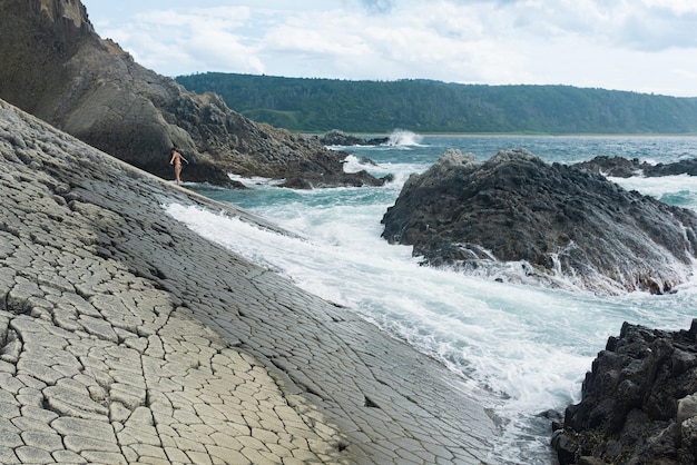 Riva in mare naturale di lava rialzata surf tra le rocce costiere che si affacciano sulla riva lontana e la donna che fa il bagno a terra