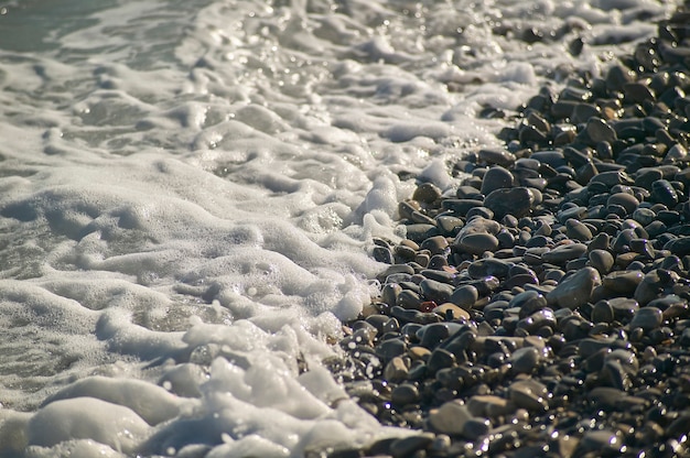 波の水が濡れた岩を打ち砕く小石のビーチの海の岸。