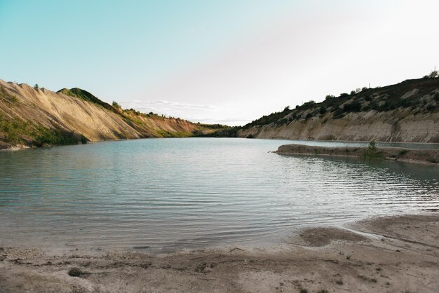 Riva con acqua azzurra turchese del primo piano dell'argilla bianca nel lago poco profondo dello stagno con superficie luminosa dell'acqua blu chiara