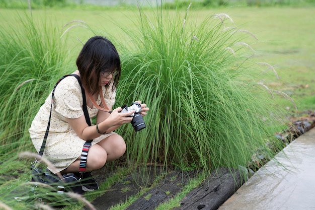 Short hair woman sit near green grass flower in garden looking at camera display to see preview picture