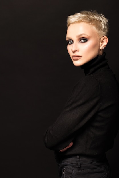 Short-haired blonde in black clothes on a black wall.