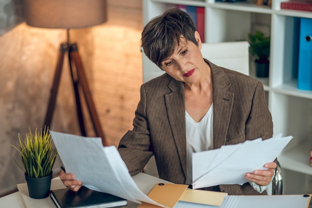 Short-haired businesswoman sitting in the office and working with papers