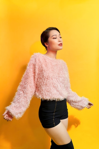 Short-haired girl in fashionable dancing. Young playful female model in stylish fur outfit. Beautiful happy woman having fun dance in studio on yellow