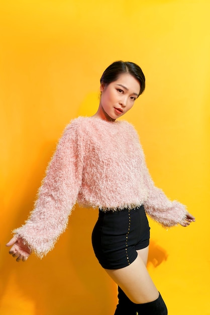 Short-haired girl in fashionable dancing. Young playful female model in stylish fur outfit. Beautiful happy woman having fun dance in studio on yellow
