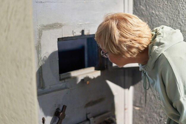 A short haired woman looks out the window of a prison cell door. a prison guard keeps order in the cell