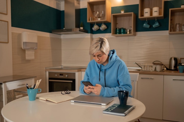 Short haired woman using smartphone in the kitchen at home