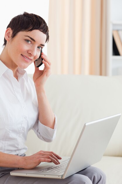 Short-haired woman with a laptop and a phone looking into the ca