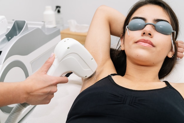 Short shot Aesthetician giving laser diode treatment to a woman in the armpit where the client wears laser protection glasses