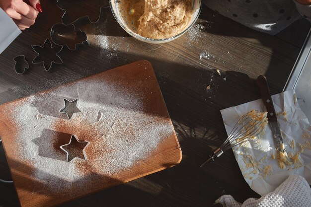 Песочное тесто для пряников, раскатанное на деревянной доске. Вырезание печенья в форме звезды.