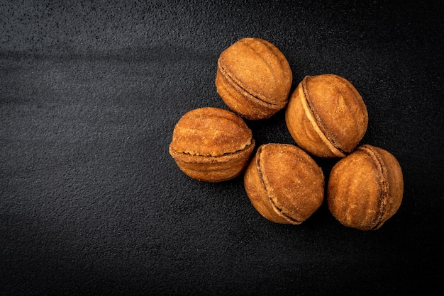 Shortbread in shape nut with caramel on black surface.