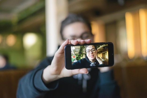 Shortcut hipster young blogger speaking in front of phone camera for vlog while sitting at the cafe