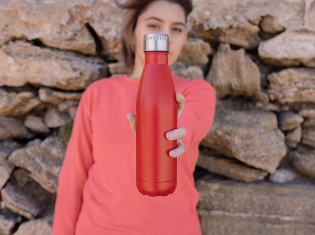 Shorthaired Teenage girl in pink hoodie staying near a stone wall with red water bottle