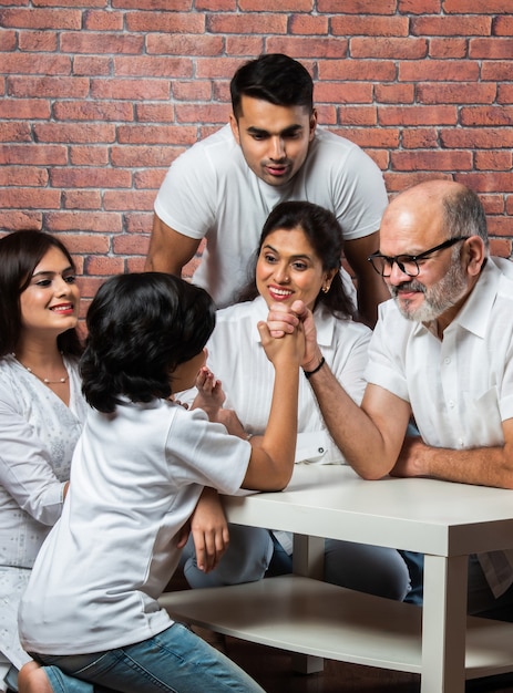 ShortPlayful Indian Asian kid and Grandfather Arm wrestling at home with other family members looking wearing white cloths