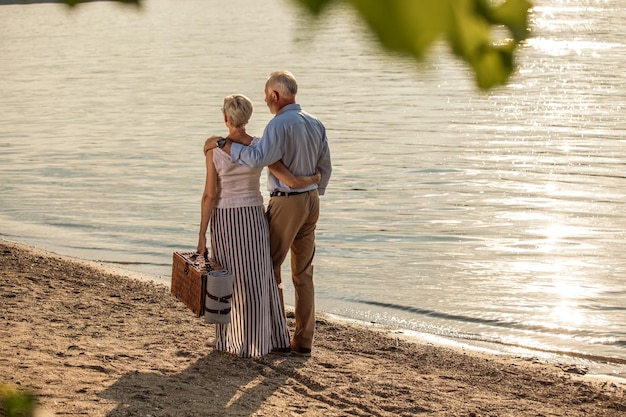 川岸でピクニックに行く愛情のこもった年配のカップルのショットバックショット