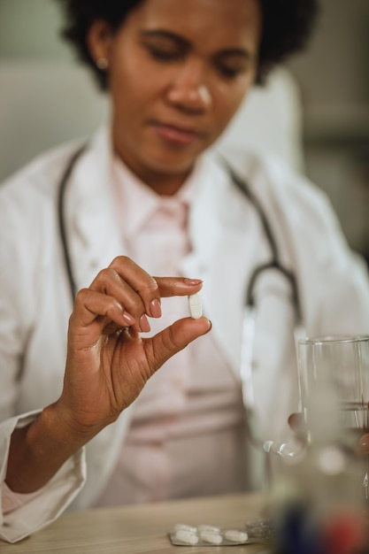 Inquadratura di una dottoressa africana che si sente stressata e assume farmaci mentre lavora nel suo ufficio durante la pandemia di covid-19.