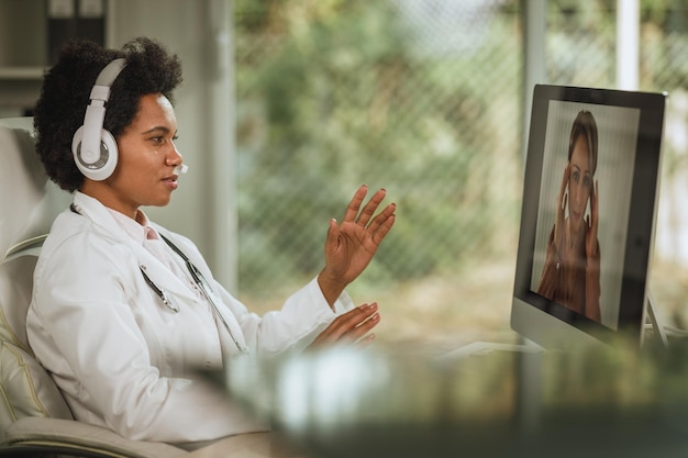 Foto inquadratura di una dottoressa africana che fa una videochiamata con un paziente al computer nella sua stanza di consultazione durante la pandemia di covid-19.