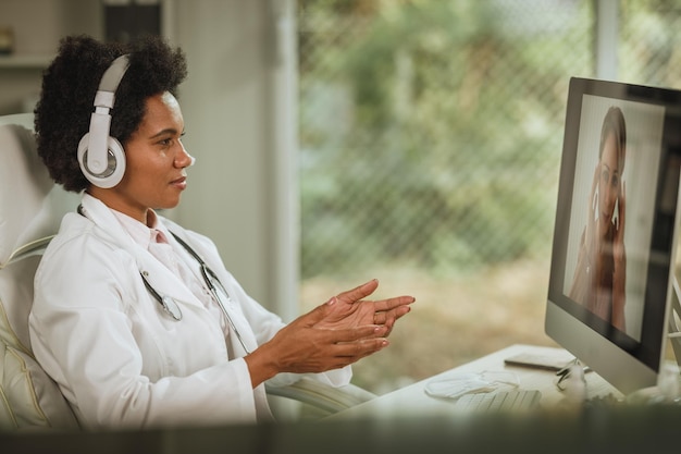 Photo shot of an african female doctor having video call with patient on computer in her consulting room during covid-19 pandemic.