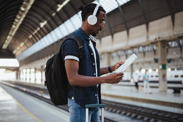 Inquadratura di un uomo africano che legge una mappa in una stazione ferroviaria sta aspettando mentre ascolta la musica