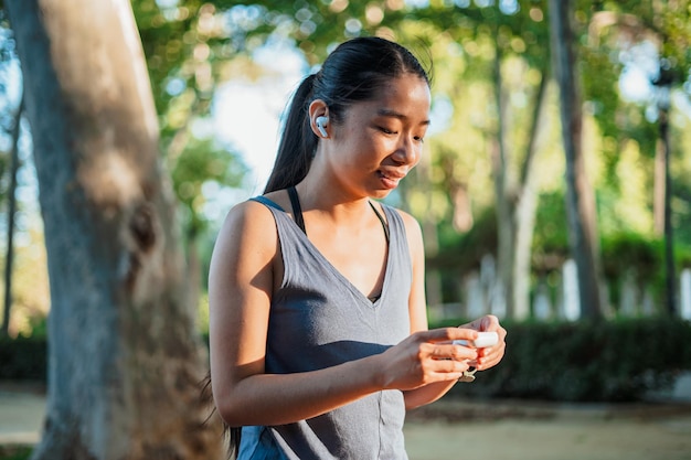 Inquadratura di una ragazza sportiva asiatica che apre la custodia di auricolari wireless prima di andare a fare jogging nel parco