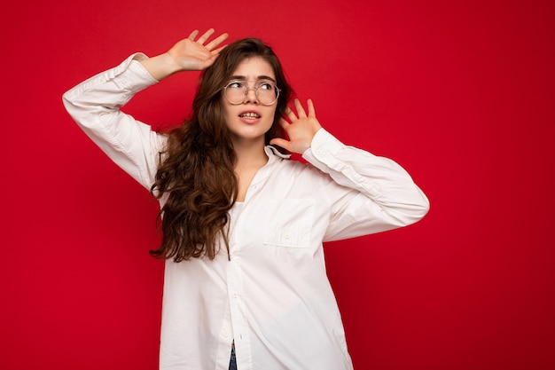 Shot of attractive angry sad dissatisfied young curly brunette female person wearing white shirt and